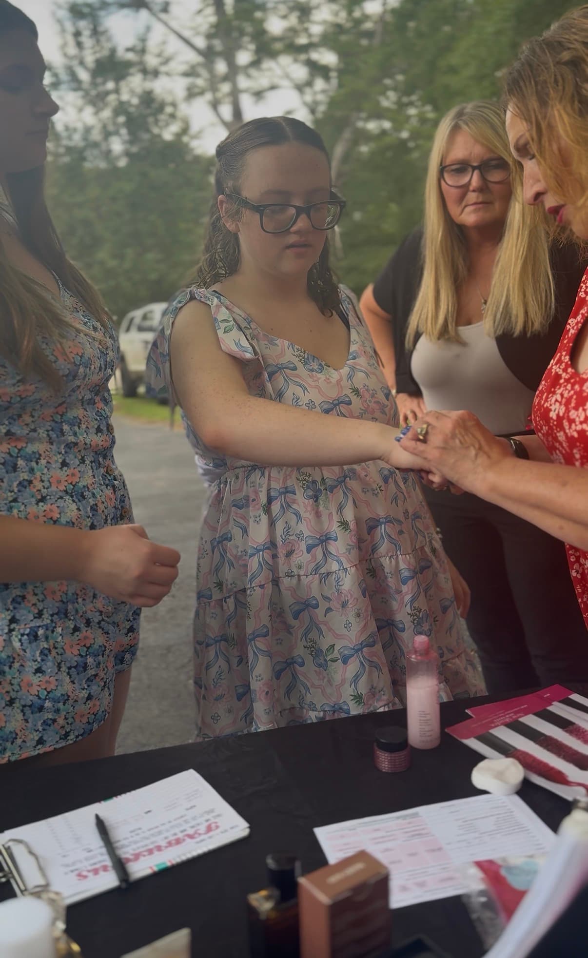 Woman in floral dress tests beauty product on her hand at an outdoor table.