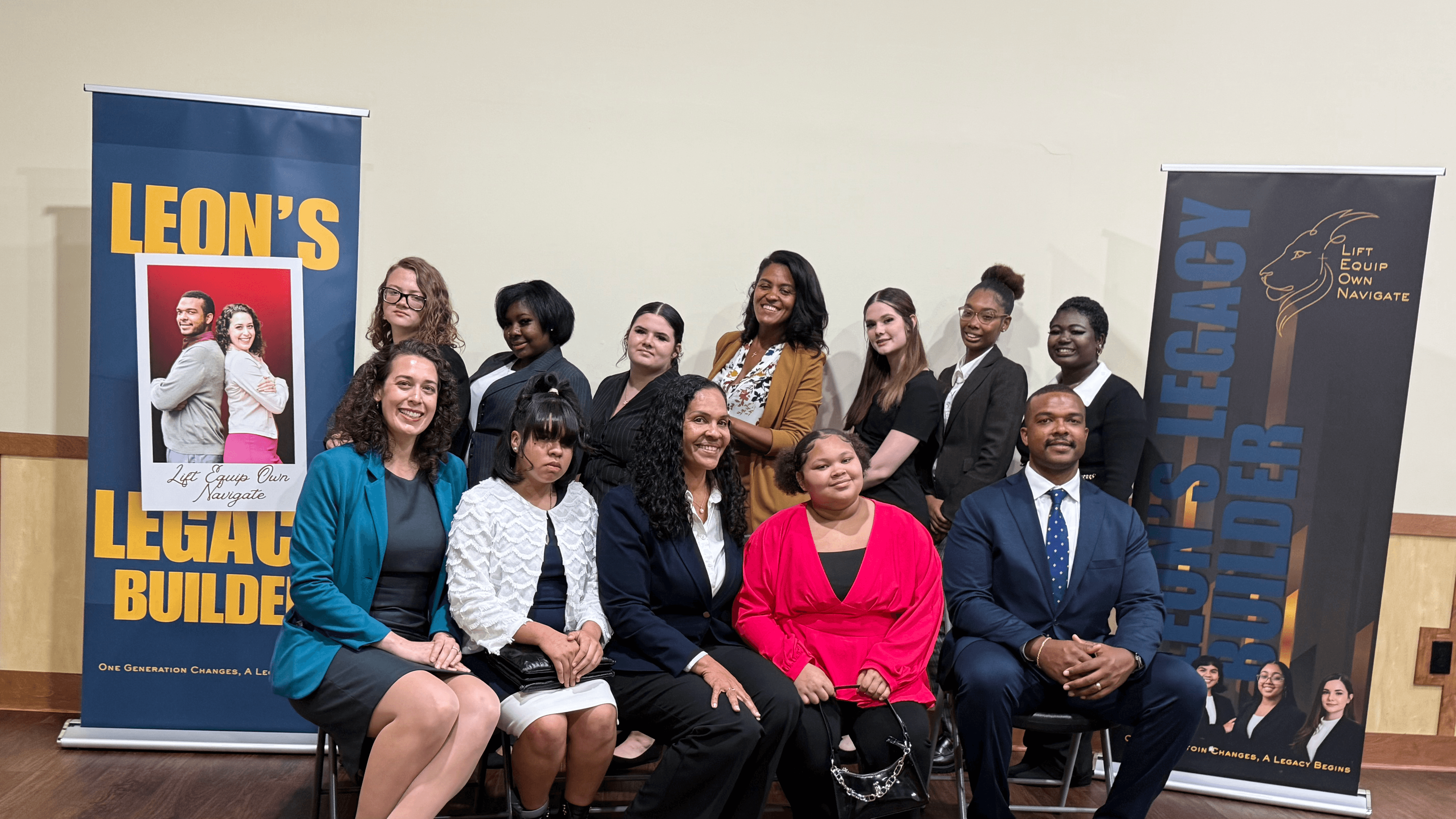 Diverse group of people in professional attire posing between two Leon's Legacy Builders banners.